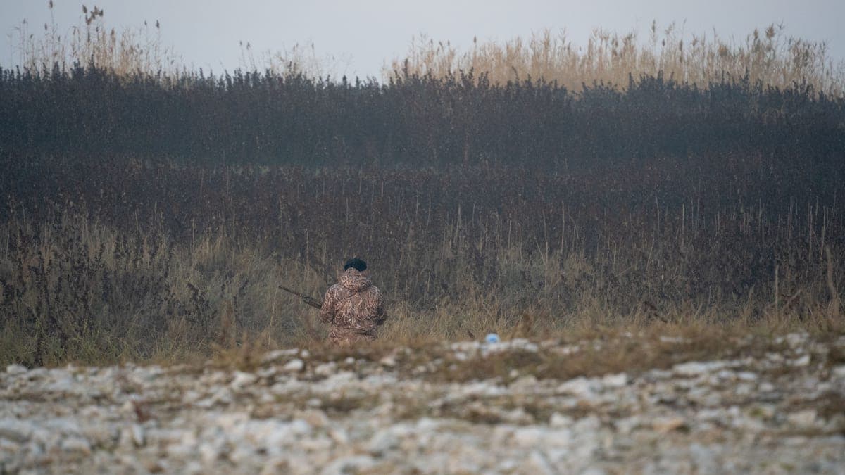 The back of a hunter in camouflage in a rural winter setting