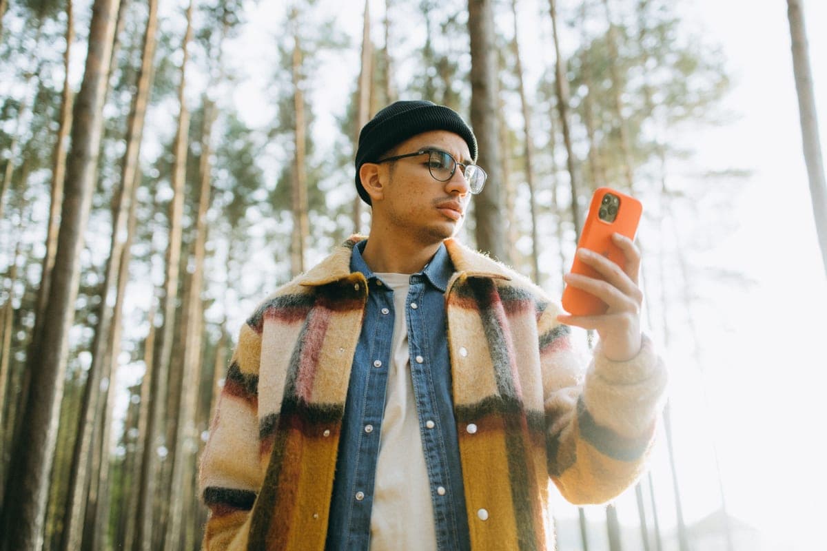 A man in a plaid coat checking his smartphone among tall forest trees