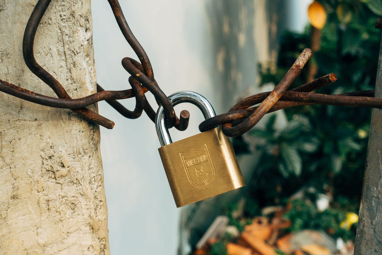 A brass padlock securing a wire to a concrete post